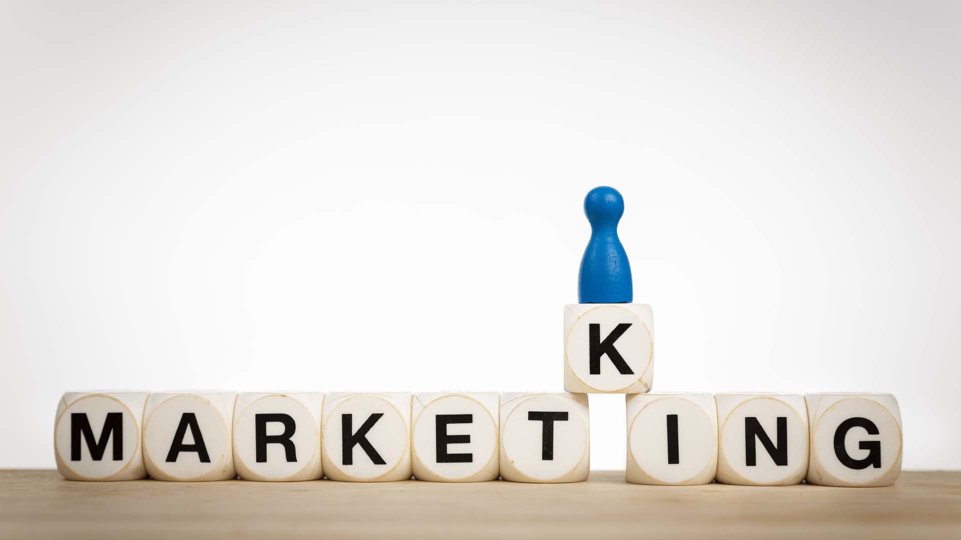 Digital Marketing Agency concept with wooden blocks spelling 'Marketing' and a blue game piece on top.