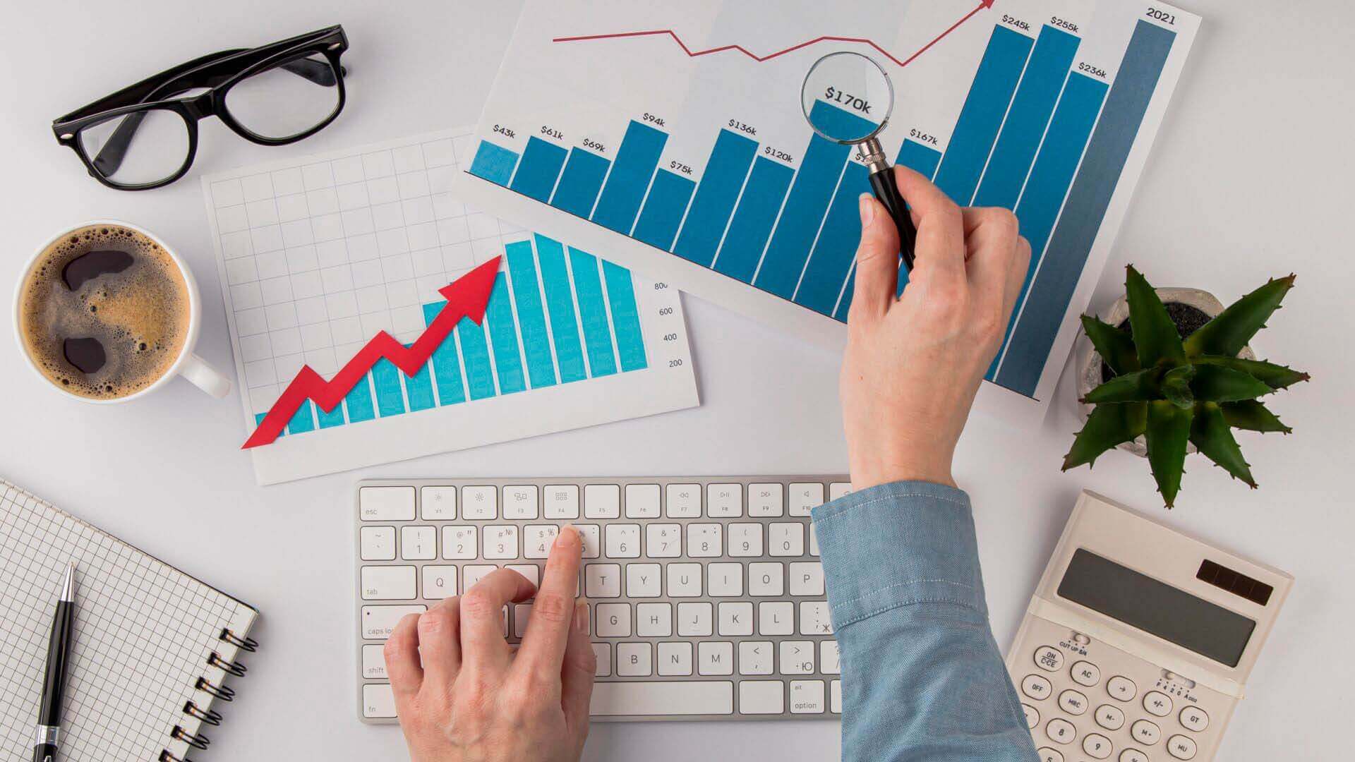 Person analyzing e-commerce business growth charts with a keyboard, coffee, and calculator.